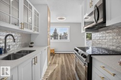 Modern kitchen with wood-finish flooring, white cabinetry, integrated stainless steel appliances, and a tile backsplash - 