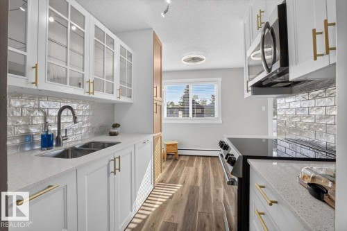 White cabinetry with gold-tone hardware, wood-finish flooring, and a subway tile backsplash - #205 11429 124 St Nw, Edmonton, AB - Indoor Photo Showing Kitchen With Double Sink With Upgraded Kitchen