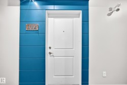White paneled entry door with satin nickel hardware, set against a blue horizontally paneled accent wall, featuring a polished metal unit number plate - 