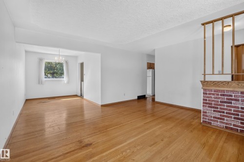 Hardwood flooring throughout, white painted walls, textured ceilings, a brick and wood room divider, and a built-in chandelier - 16009 93A Avenue Nw, Edmonton, AB - Indoor Photo Showing Other Room