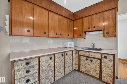Wood-finish upper cabinetry, laminate countertops, and a stainless steel sink with chrome faucet - 16009 93A Avenue Nw, Edmonton, AB - Indoor Photo Showing Other Room