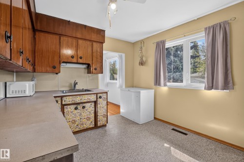 Wood cabinetry, laminate countertops, stainless steel sink, large window, and light-toned flooring - 16009 93A Avenue Nw, Edmonton, AB - Indoor Photo Showing Kitchen