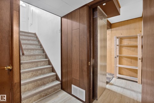 Wood-paneled wall, carpeted staircase with wood handrail, and built-in shelving unit - 16009 93A Avenue Nw, Edmonton, AB - Indoor Photo Showing Other Room