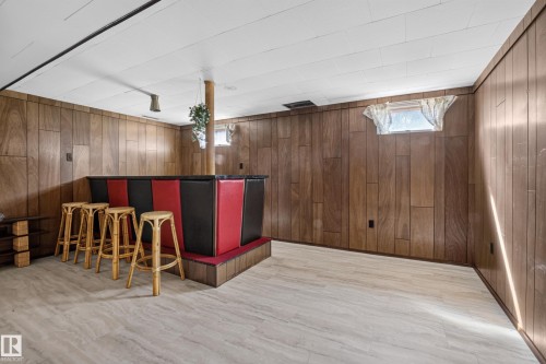 Finished room featuring wood-paneled walls, light-toned flooring, and a built-in bar with red and black paneling - 16009 93A Avenue Nw, Edmonton, AB - Indoor