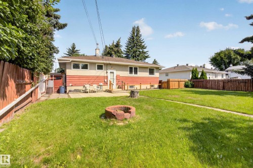 Expansive grass yard with wood fencing, mature trees, and a concrete patio - 16009 93A Avenue Nw, Edmonton, AB - Outdoor