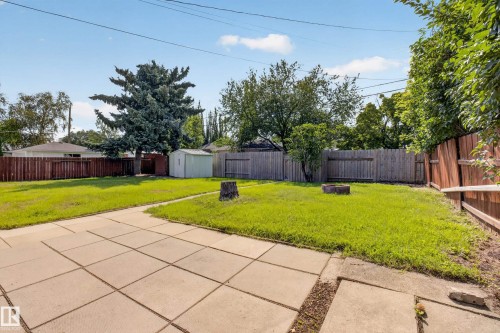 Expansive backyard with a concrete patio, mature trees, wood fencing, and a storage shed - 16009 93A Avenue Nw, Edmonton, AB - Outdoor With Backyard