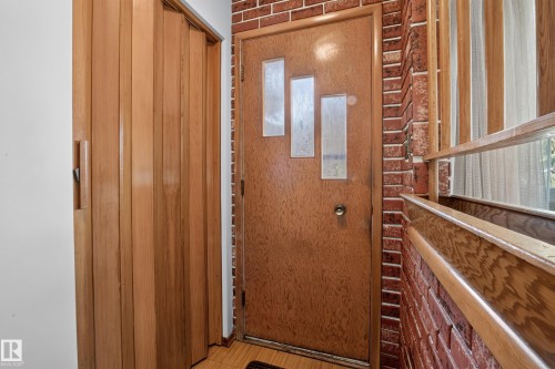 Wood-finish accordion door, brick wall accent, wood-finish entry door with three frosted glass panels, wood-finish window frame - 16009 93A Avenue Nw, Edmonton, AB - Indoor Photo Showing Other Room