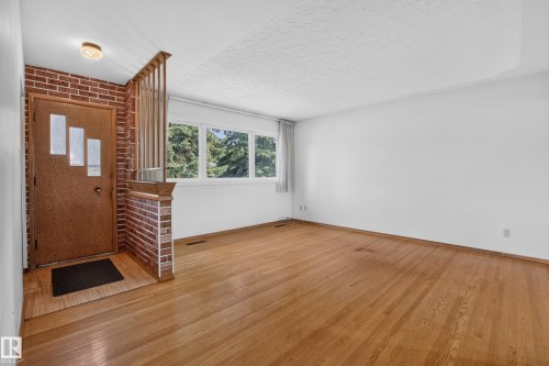 Wood-finish flooring, brick accent wall, wood door with decorative glass inserts, and a three-lite window. - 16009 93A Avenue Nw, Edmonton, AB - Indoor Photo Showing Other Room