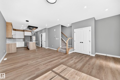 Open-concept living area featuring warm wood-finish flooring, recessed ceiling lighting, and a modern kitchen with light cabinetry and island - 426 Crystal Creek Link, Leduc, AB - Indoor Photo Showing Other Room