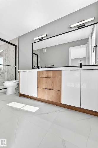 Dual vanity with white and wood-finish cabinetry, a large frameless mirror, and overhead linear light fixtures - 426 Crystal Creek Link, Leduc, AB - 