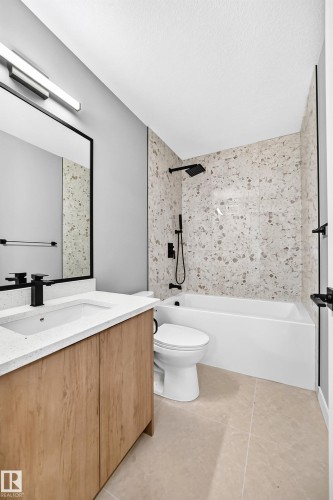 Wood-finish vanity with a white countertop and integrated sink, matte black faucet, full-width mirror, light-toned floor tile, and a tiled shower surround with a matte black shower head and controls - 426 Crystal Creek Link, Leduc, AB - Indoor Photo Showing Bathroom