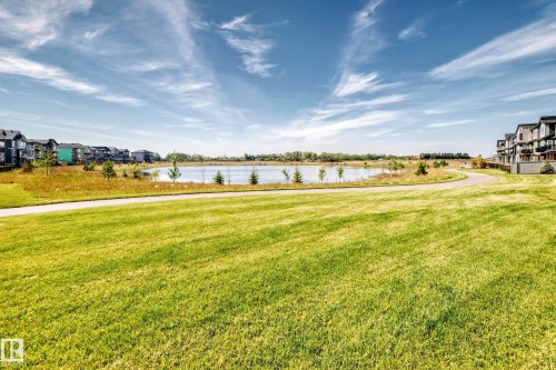 Expansive green space featuring a paved pathway, a tranquil pond, and contemporary multi-story residences - 426 Crystal Creek Link, Leduc, AB - Outdoor With View