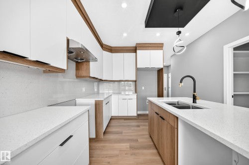 Kitchen featuring white cabinetry, wood-finish accents, white countertops, stainless steel range hood, and wood-finish flooring - 426 Crystal Creek Link, Leduc, AB - Indoor Photo Showing Kitchen With Double Sink With Upgraded Kitchen