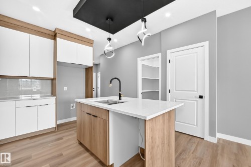 Modern kitchen featuring a central island with a sink, white countertop, and wood-finish cabinetry - 426 Crystal Creek Link, Leduc, AB - Indoor Photo Showing Kitchen With Double Sink