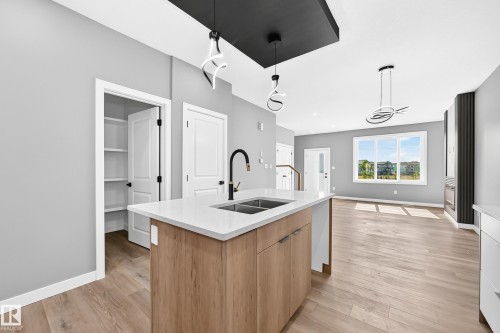 Kitchen island with a white countertop and wood-finish cabinetry - 426 Crystal Creek Link, Leduc, AB - Indoor Photo Showing Kitchen With Double Sink
