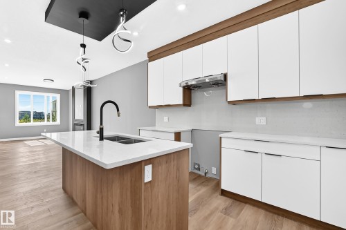 Kitchen island with a built-in sink and matte black faucet, complemented by white countertops and wood-finish cabinetry - 426 Crystal Creek Link, Leduc, AB - Indoor Photo Showing Kitchen With Double Sink