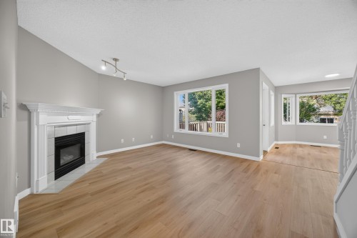 Living area with wood-finish flooring, a fireplace featuring a white mantel and tile surround, large windows, and track lighting - 3640 31 Street Nw, Edmonton, AB - Indoor Photo Showing Living Room With Fireplace