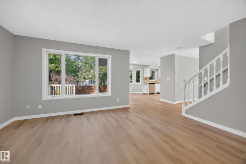 Expansive room with wood-finish flooring, large multi-pane window, and a painted staircase with white balusters - 3640 31 Street Nw, Edmonton, AB - Indoor