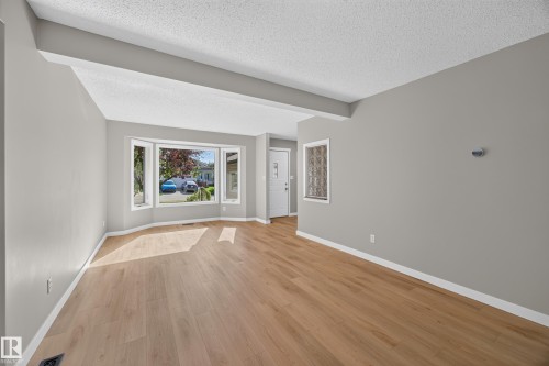 Spacious room featuring wood-finish flooring, a bay window, a textured ceiling, and a white entry door - 3640 31 Street Nw, Edmonton, AB - Indoor Photo Showing Other Room