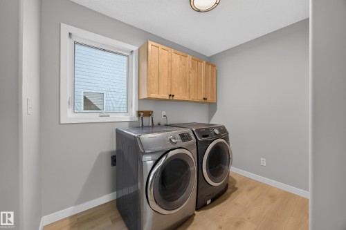 Laundry area featuring wood-finish flooring, light gray walls, a window with white trim, and built-in wood cabinetry - 3640 31 Street Nw, Edmonton, AB - Indoor Photo Showing Laundry Room