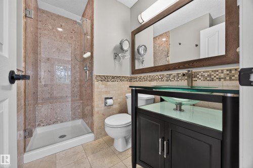 Glass-enclosed shower with a built-in bench, a vessel sink vanity, a framed mirror, and mosaic tile accents - 3640 31 Street Nw, Edmonton, AB - Indoor Photo Showing Bathroom