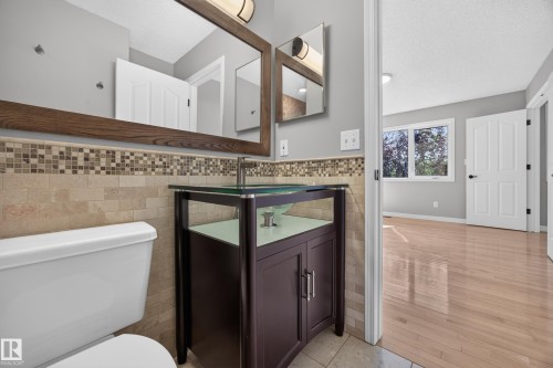 Bathroom vanity with a glass vessel sink, mosaic tile backsplash, and a large wood-framed mirror - 3640 31 Street Nw, Edmonton, AB - Indoor Photo Showing Bathroom