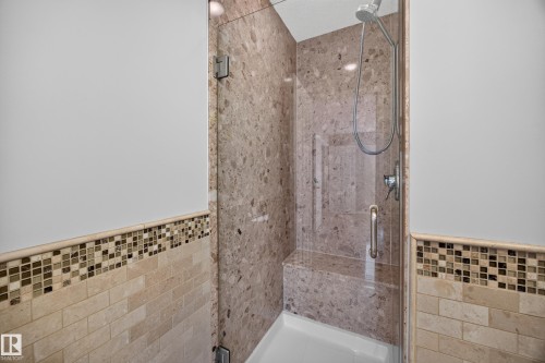 Glass-enclosed shower with stone-look tile walls, a built-in bench, and a mosaic tile accent - 3640 31 Street Nw, Edmonton, AB - Indoor Photo Showing Bathroom