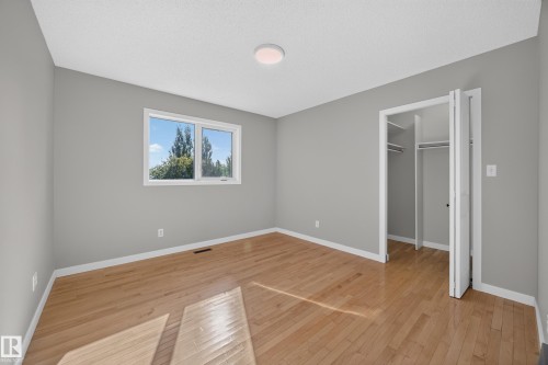 Bedroom 2.  Hardwood flooring, light gray wall finish, white trim, double-door closet with built-in shelving, and a prominent window - 3640 31 Street Nw, Edmonton, AB - Indoor Photo Showing Other Room