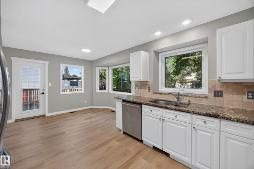 Kitchen featuring white cabinetry, granite countertops, tile backsplash, stainless steel dishwasher, and wood-finish flooring - 3640 31 Street Nw, Edmonton, AB - Indoor Photo Showing Kitchen With Double Sink