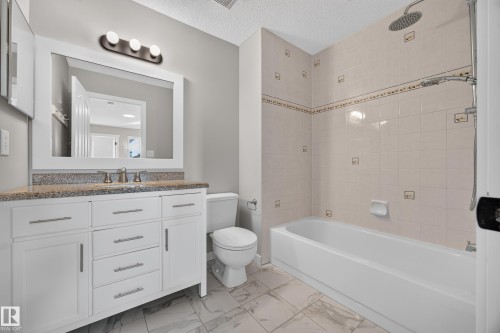 White vanity with a speckled countertop, undermount sink, and brushed nickel faucet - 3640 31 Street Nw, Edmonton, AB - Indoor Photo Showing Bathroom