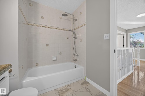 Bathtub with tiled surround, rain shower head, and an additional handheld shower fixture - 3640 31 Street Nw, Edmonton, AB - Indoor Photo Showing Bathroom