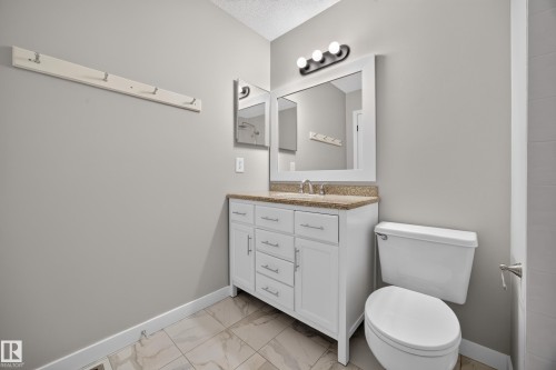 White vanity with a stone-finish countertop, under-mount sink, and framed mirror - 3640 31 Street Nw, Edmonton, AB - Indoor Photo Showing Bathroom