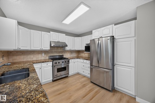 White cabinetry, stainless steel appliances, wood-finish flooring, stone-finish countertops, and a tile backsplash - 3640 31 Street Nw, Edmonton, AB - Indoor Photo Showing Kitchen With Stainless Steel Kitchen With Double Sink