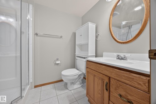 Bathroom featuring a vanity with a white countertop, wood-finish cabinetry, a round wood-framed mirror, and tiled flooring - 3640 31 Street Nw, Edmonton, AB - Indoor Photo Showing Bathroom
