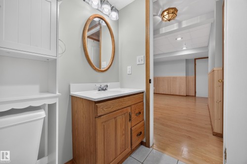 Wood-finish vanity with a white countertop and oval mirror, complemented by a white storage cabinet - 3640 31 Street Nw, Edmonton, AB - Indoor Photo Showing Bathroom
