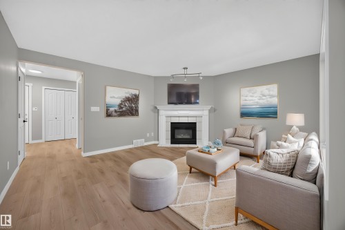 Light wood-finish flooring, corner fireplace with white mantel, track lighting fixture, light gray wall paint, and white trim throughout - 3640 31 Street Nw, Edmonton, AB - Indoor Photo Showing Living Room With Fireplace