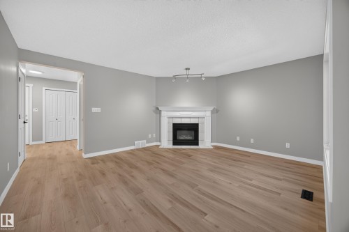 Wood-finish flooring, white trim, gas fireplace with white mantel, track lighting, and neutral wall tones - 3640 31 Street Nw, Edmonton, AB - Indoor Photo Showing Living Room With Fireplace