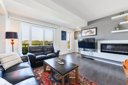 Spacious living area featuring wood-finish flooring, a built-in electric fireplace, and a sliding glass door to an outdoor balcony - 8265 Chappelle Way Sw, Edmonton, AB - Indoor Photo Showing Living Room With Fireplace