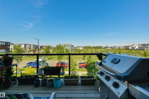 Wood-finish outdoor deck with a glass and metal railing, overlooking a green space and residential area - 8265 Chappelle Way Sw, Edmonton, AB - Outdoor With Deck Patio Veranda
