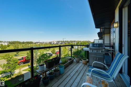 Outdoor deck with wood-finish flooring, glass panel railing, and exterior wall lighting - 8265 Chappelle Way Sw, Edmonton, AB - Outdoor With Exterior