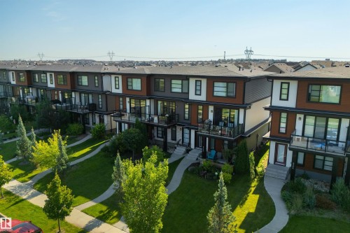 Contemporary multi-level townhomes featuring private balconies, individual entrances, manicured green spaces, and paved walkways - 8265 Chappelle Way Sw, Edmonton, AB - Outdoor With Facade