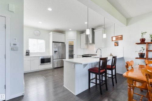 Kitchen featuring white cabinetry, stainless steel appliances, a center island with seating, and wood-finish flooring - 8265 Chappelle Way Sw, Edmonton, AB - Indoor Photo Showing Kitchen With Upgraded Kitchen