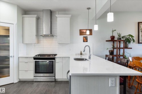 Kitchen featuring stainless steel appliances, white cabinetry, white countertops, white subway tile backsplash, and wood-finish flooring - 8265 Chappelle Way Sw, Edmonton, AB - Indoor Photo Showing Kitchen With Double Sink With Upgraded Kitchen