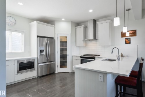 Modern kitchen with stainless steel appliances, white cabinetry, a built-in microwave, and a breakfast bar island - 8265 Chappelle Way Sw, Edmonton, AB - Indoor Photo Showing Kitchen With Stainless Steel Kitchen With Upgraded Kitchen