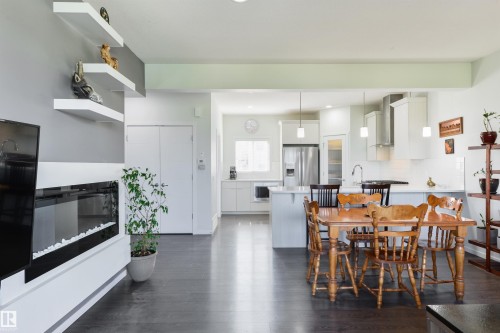 Integrated living space featuring wood-finish flooring, a built-in fireplace, white floating shelves, recessed lighting, and a kitchen with white cabinetry - 8265 Chappelle Way Sw, Edmonton, AB - Indoor With Fireplace