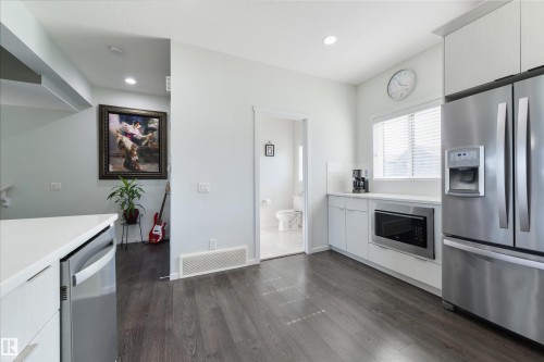 Kitchen featuring wood-finish flooring, white cabinetry, stainless steel appliances, and a built-in microwave - 8265 Chappelle Way Sw, Edmonton, AB - Indoor Photo Showing Kitchen