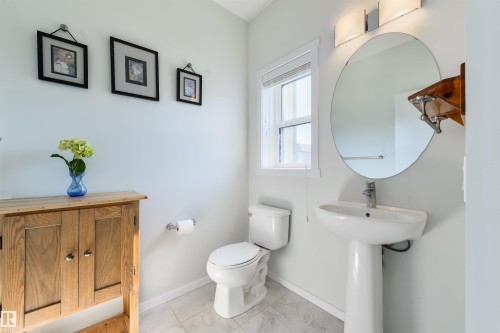 Pedestal sink with single-handle faucet, round wall-mounted mirror, and wall-mounted light fixture - 8265 Chappelle Way Sw, Edmonton, AB - Indoor Photo Showing Bathroom