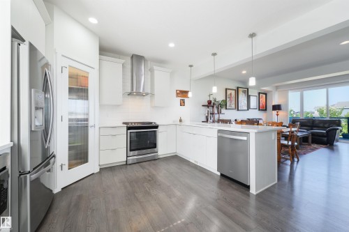 Modern kitchen featuring stainless steel appliances, wood-finish flooring, white cabinetry, a large kitchen island, and recessed lighting - 8265 Chappelle Way Sw, Edmonton, AB - Indoor Photo Showing Kitchen With Stainless Steel Kitchen With Upgraded Kitchen