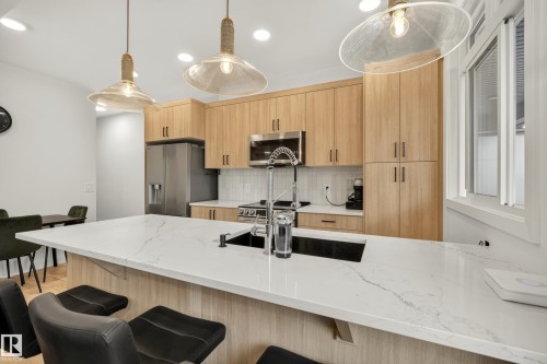 Kitchen featuring light wood-finish cabinetry, stainless steel appliances, a white tile backsplash, a large center island with a sink, and pendant lighting - #53 16231 19 Av Sw, Edmonton, AB - Indoor Photo Showing Kitchen