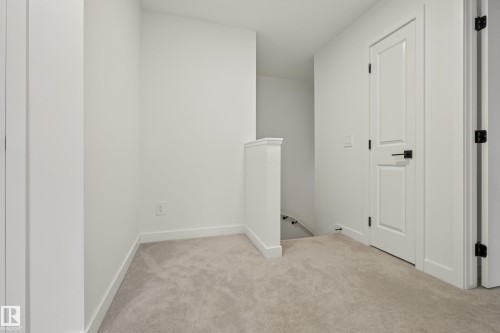 Neutral-toned carpeting throughout, crisp white walls, and a white panel door with matte black hardware - #53 16231 19 Av Sw, Edmonton, AB - Indoor Photo Showing Other Room